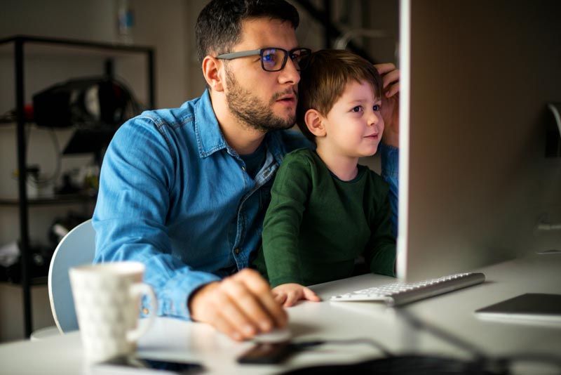 A father in a jean shirt sitting at his computer with son